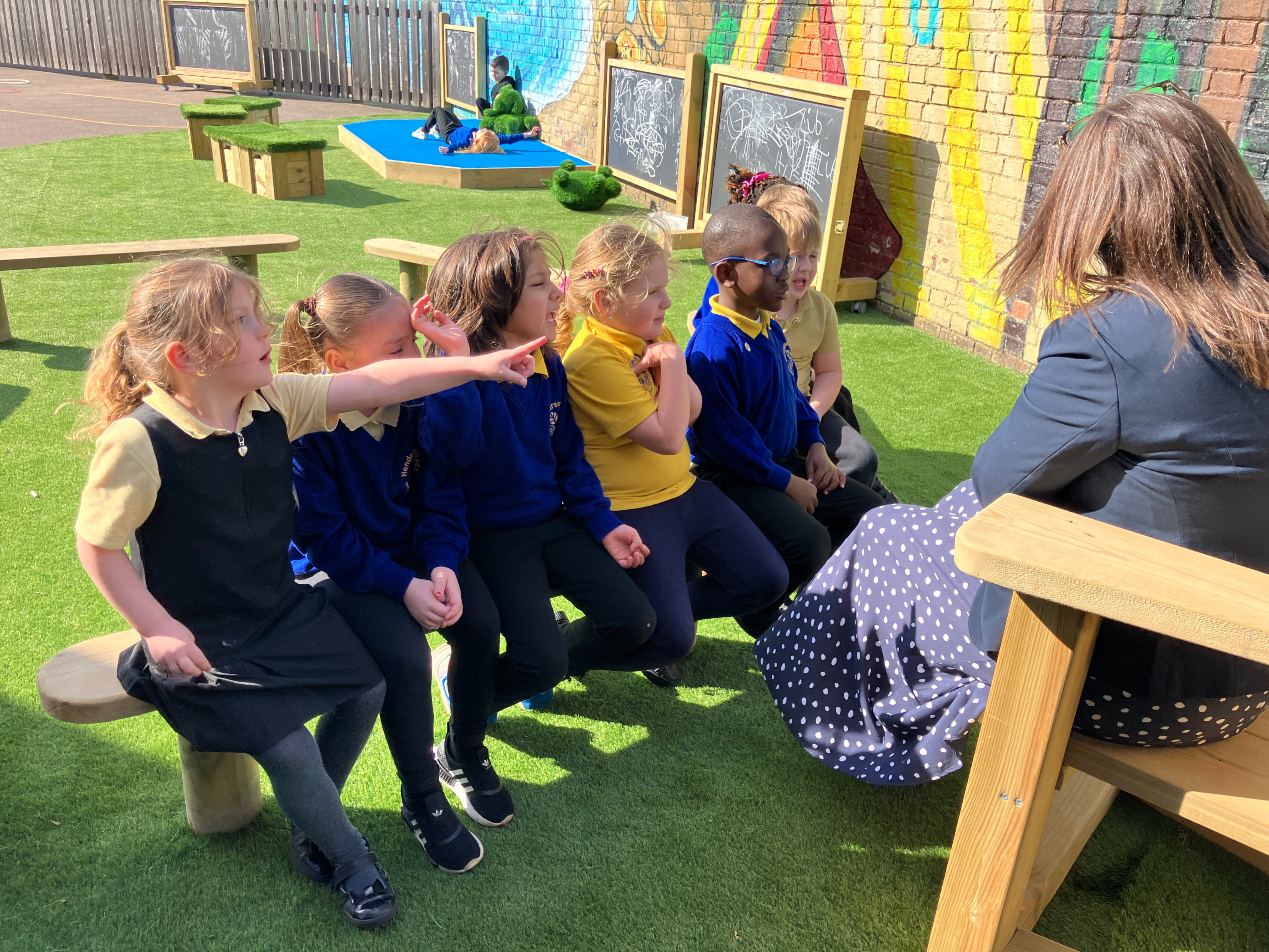 Playground layout ideas: storytelling area with children enjoying reading with their teacher