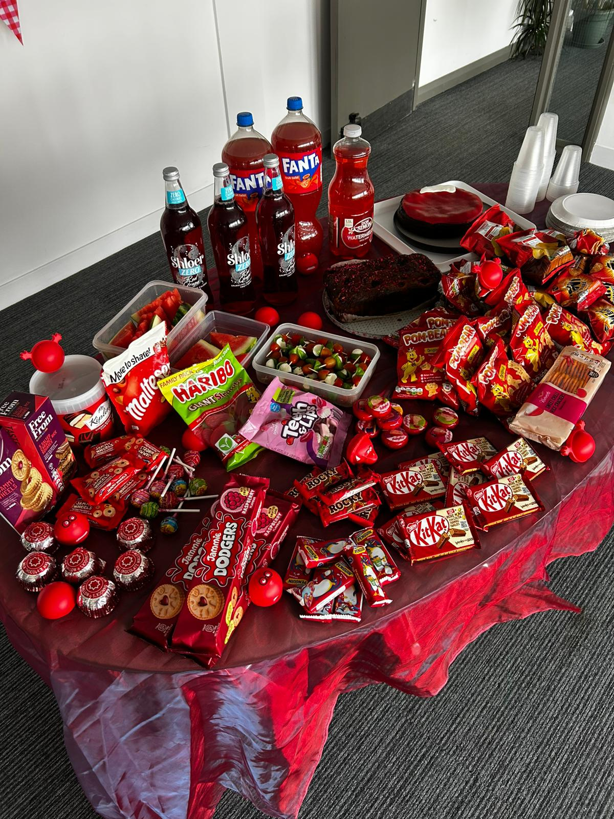 Comic Relief bake sale table stocked with red foods and drinks